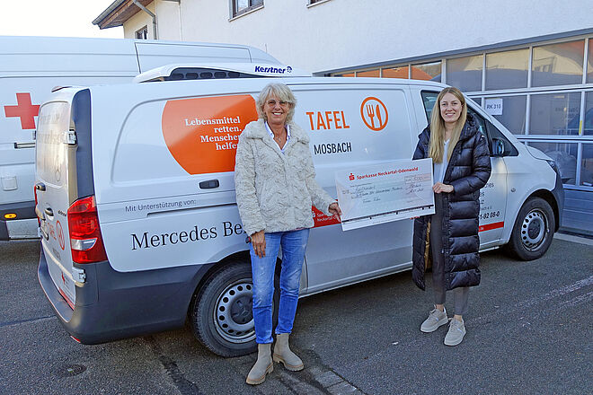 Vor dem Fahrzeug des Tafelladens halten Manuela Schönig vom Tafelladen und Janine Horn von FIBRO einen symbolischen Scheck über 500 Euro in den Händen.